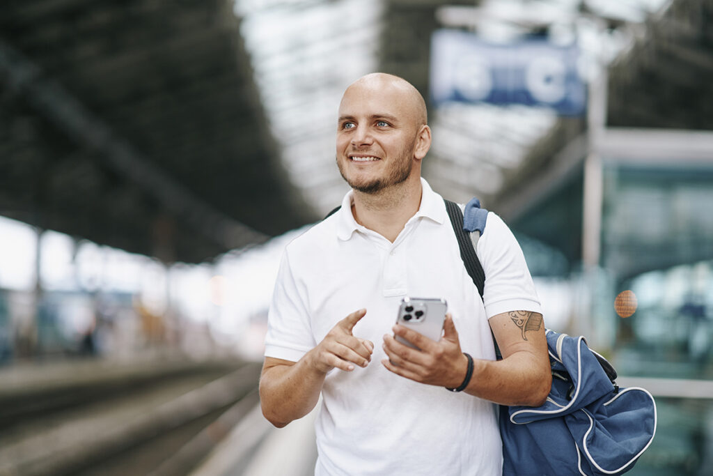 Ein Mann in einem Bahnhof mit einem Smartphone in der Hand.