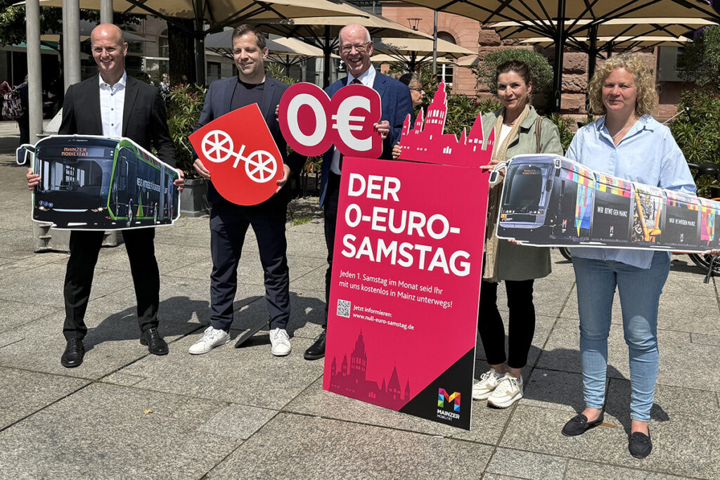 Mehrere Menschen halten Schilder mit Aufschriften zum 0-Euro-Ticket und mit Bildern hoch.