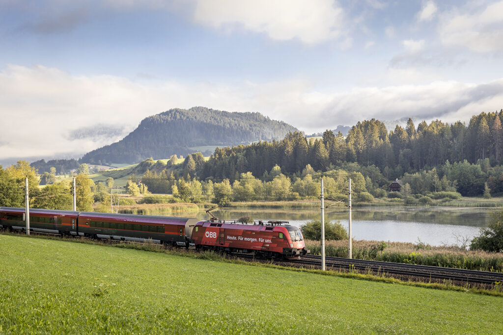 Ein Zug vor einem See und vor Bergen in Österreich.