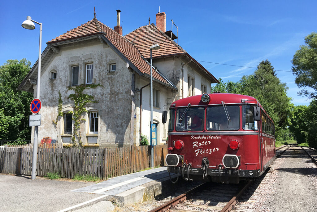 Ein Triebwagen steht vor einem Bahnhofsgebäude.