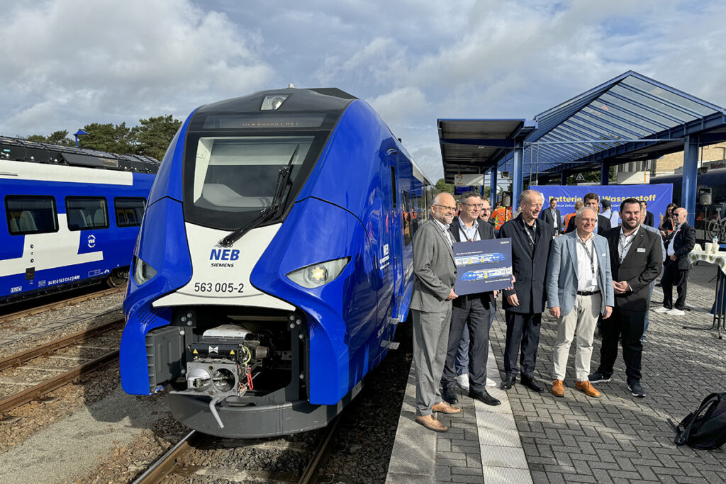 Mehrere Personen stehen vor einem Zug auf einem Bahnsteig.