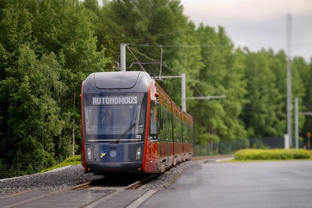 Eine automatische Straßenbahn auf einem Gleis vor Bäumen.