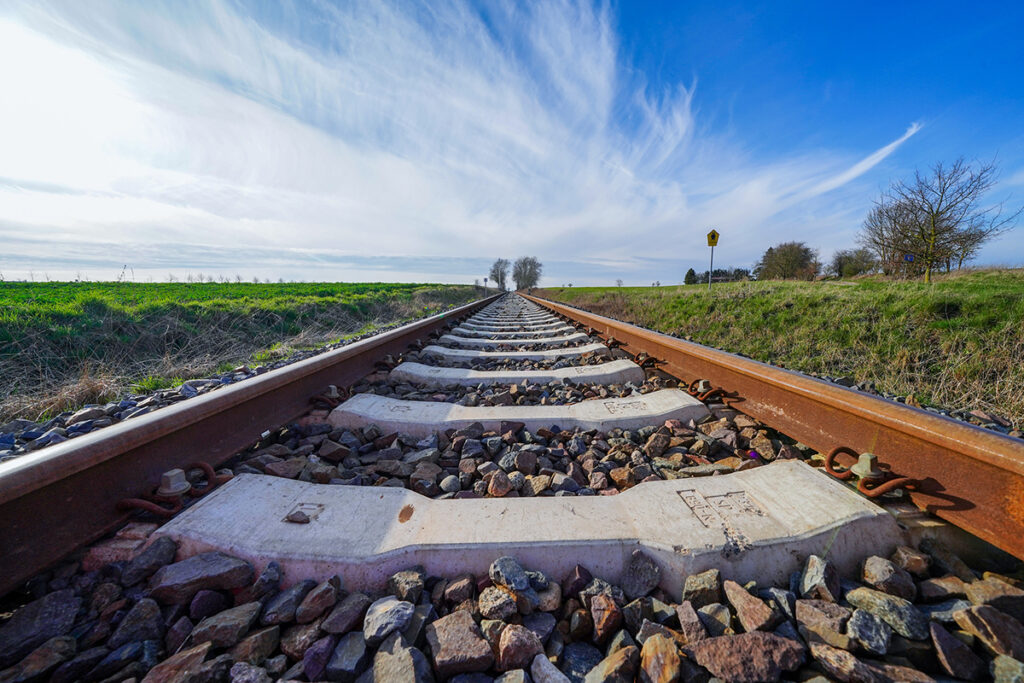 Eine eingleisige Bahnstrecke führt durch Wiesen.