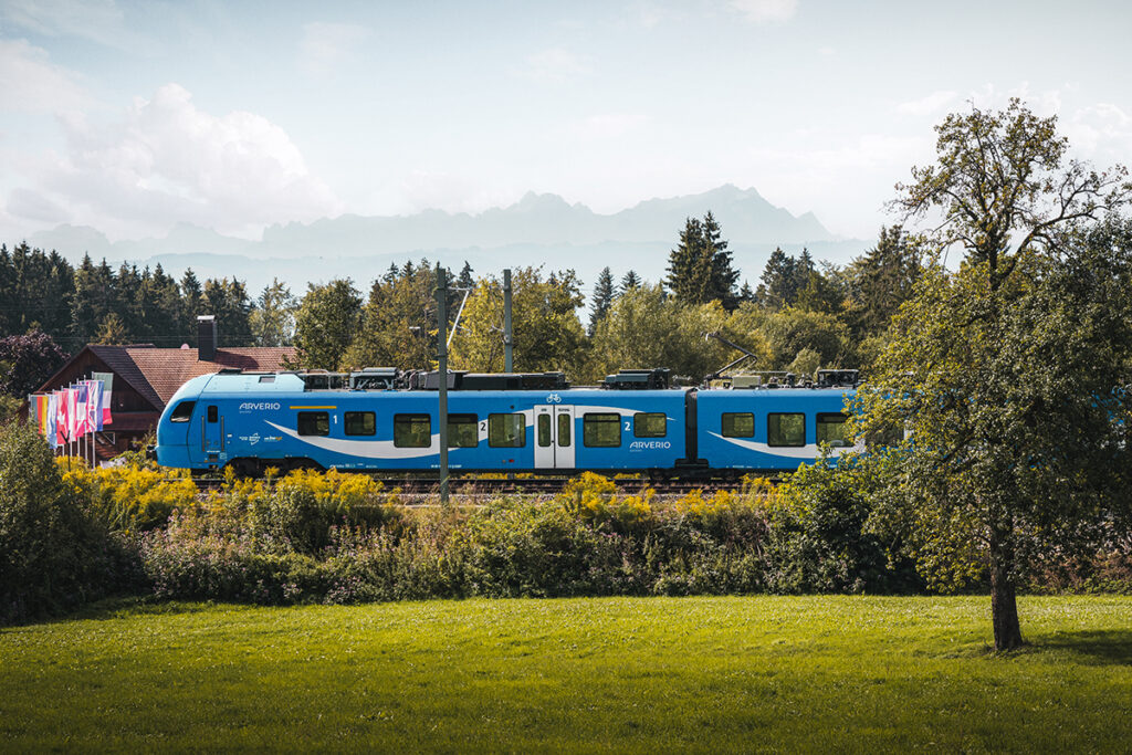 Ein Zug fährt an Bäumen und Bergen vorbei.