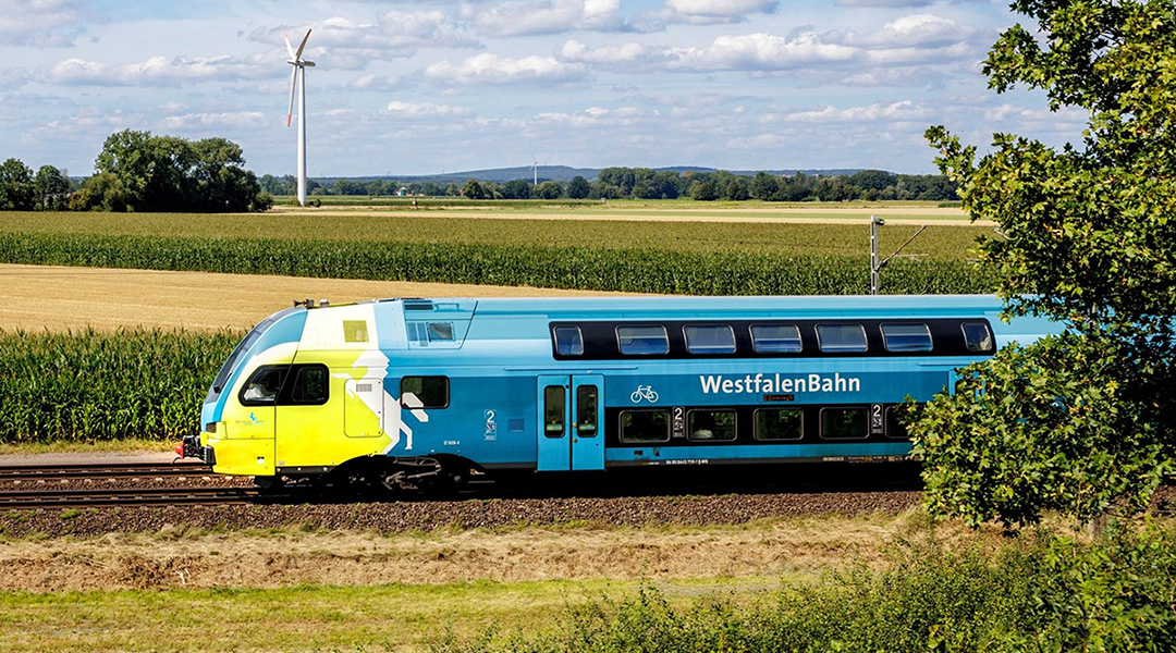 Ein Doppelstockzug fährt an Feldern vorbei.