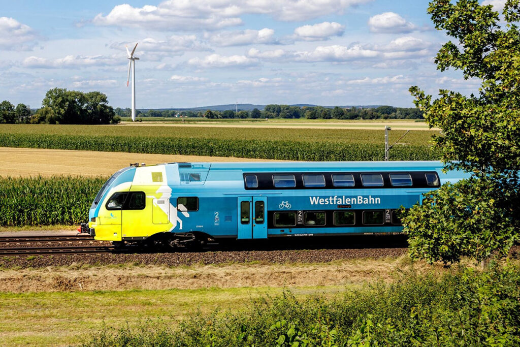 Ein Doppelstockzug fährt an Feldern vorbei.