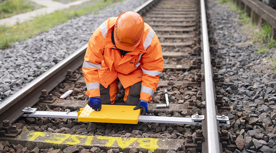 Ein Bahn-Mitarbeiter montiert eine Balise zwischen den Gleisen.