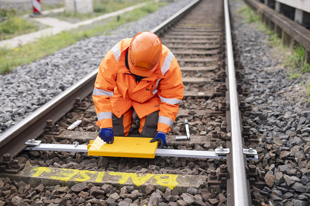 Ein Bahn-Mitarbeiter montiert eine Balise zwischen den Gleisen.