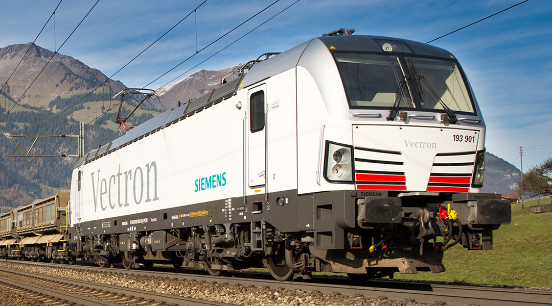 Eine Vectron-Lokomotive fährt mit einem Güterzug durch Berge.