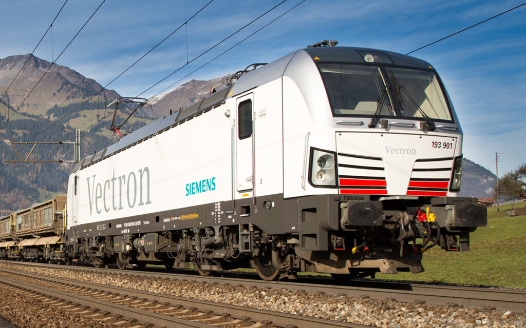 Eine Vectron-Lokomotive fährt mit einem Güterzug durch Berge.