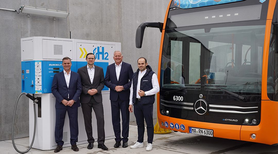 Vier Personen stehen an einer Tankstelle vor einem Bus.