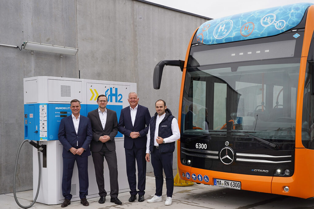 Vier Personen stehen an einer Tankstelle vor einem Bus.