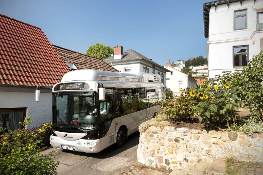 Ein elektrischer Midibus fährt auf einer schmalen Straße. 