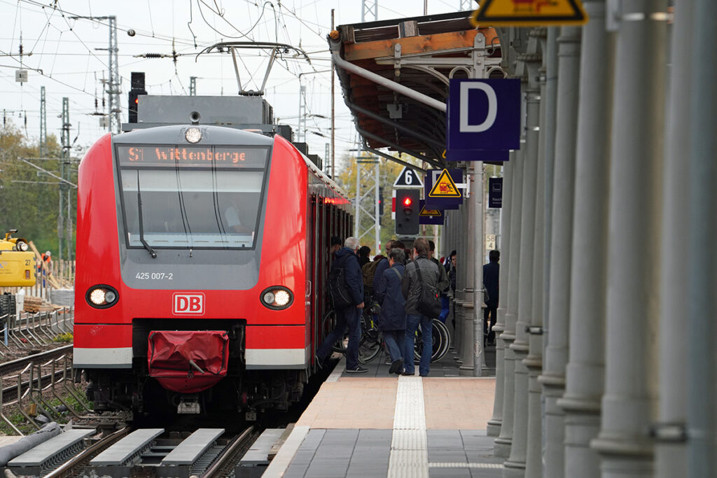 Ein S-Bahn-Zug hält an einem Bahnsteig, auf dem Menschen stehen.