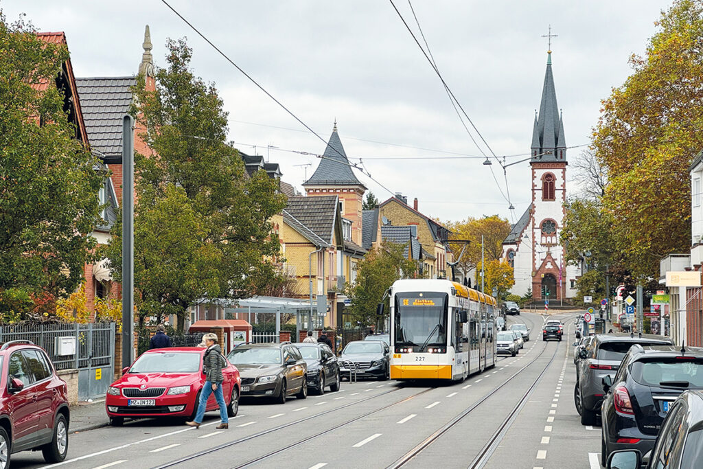 Eine Straßenbahn fährt vor Häusern und einer Kirche.