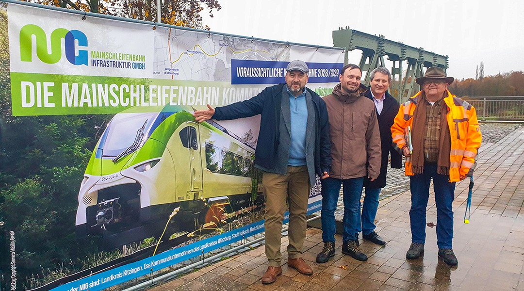 Vier Personen stehen vor einer Plakatwand.