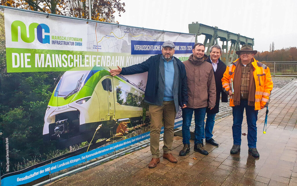 Vier Personen stehen vor einer Plakatwand.