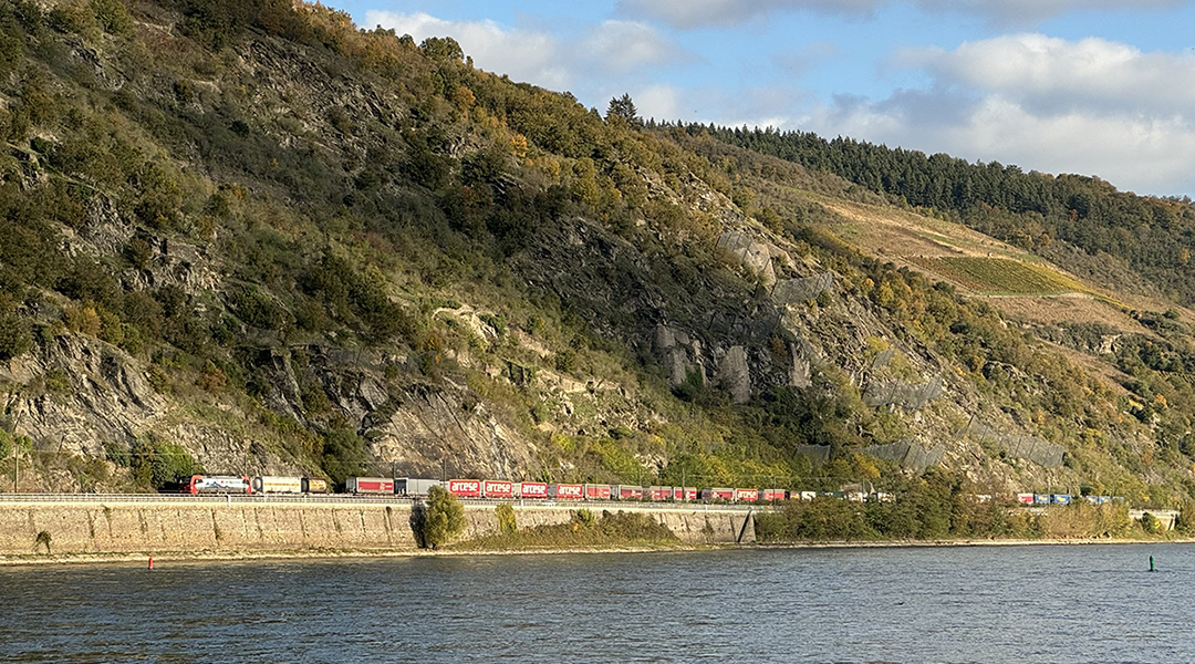 Ein Güterzug fährt vor Bergen am Rhein entlang.