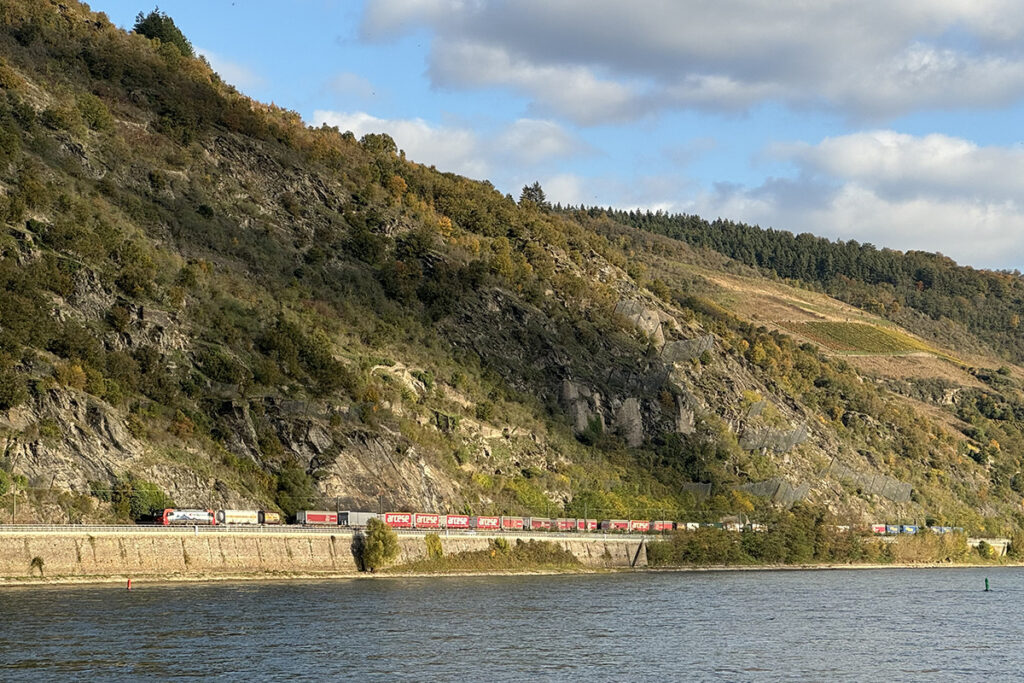 Ein Güterzug fährt vor Bergen am Rhein entlang.