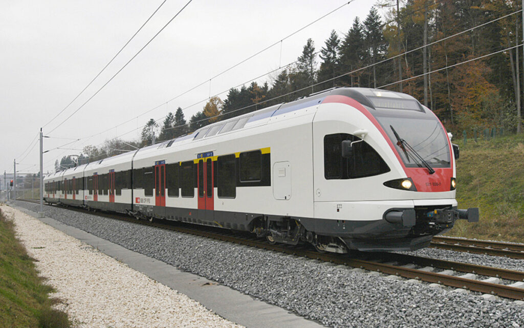 Ein Triebzug aus der Schweiz fährt durch einen Wald.