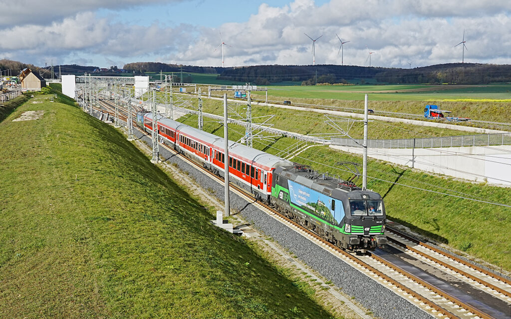 Ein Zug fährt auf einer Bahnstrecke durch Wiesen.