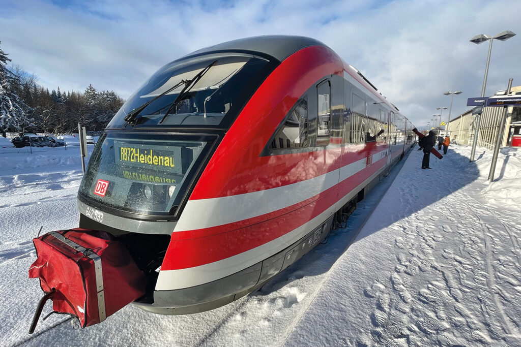 Ein Zug steht an einem Bahnsteig, auf dem Schnee liegt.