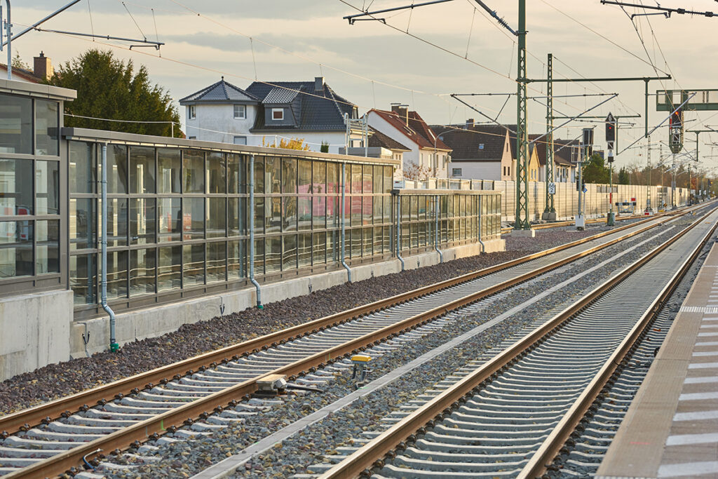 Gleise führen an einer Lärmschutzwand und einem Bahnsteig vorbei.