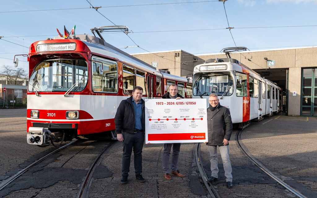 Drei Personen stehen vor zwei Stadtbahnen.