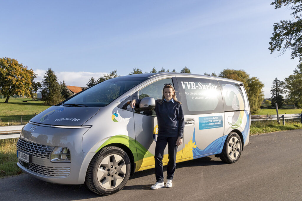 Eine Person steht vor einem elektrischen Minibus.