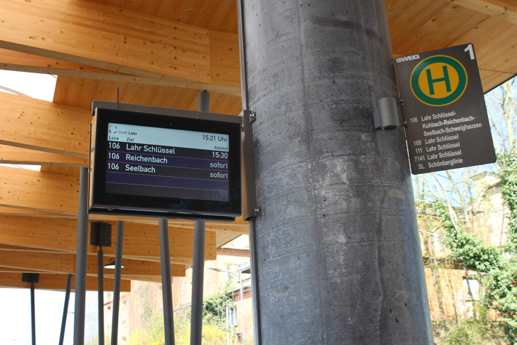 Ein Haltestellenanzeiger hängt unter einer Überdachung.