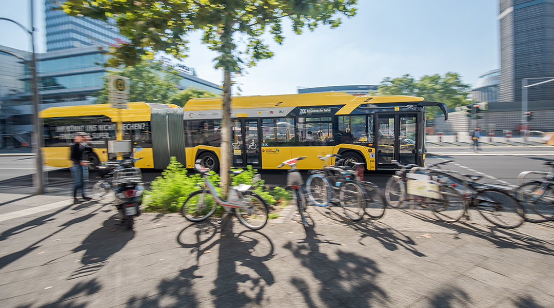 Ein Bus fährt auf einer Straße hinter einem Baum.