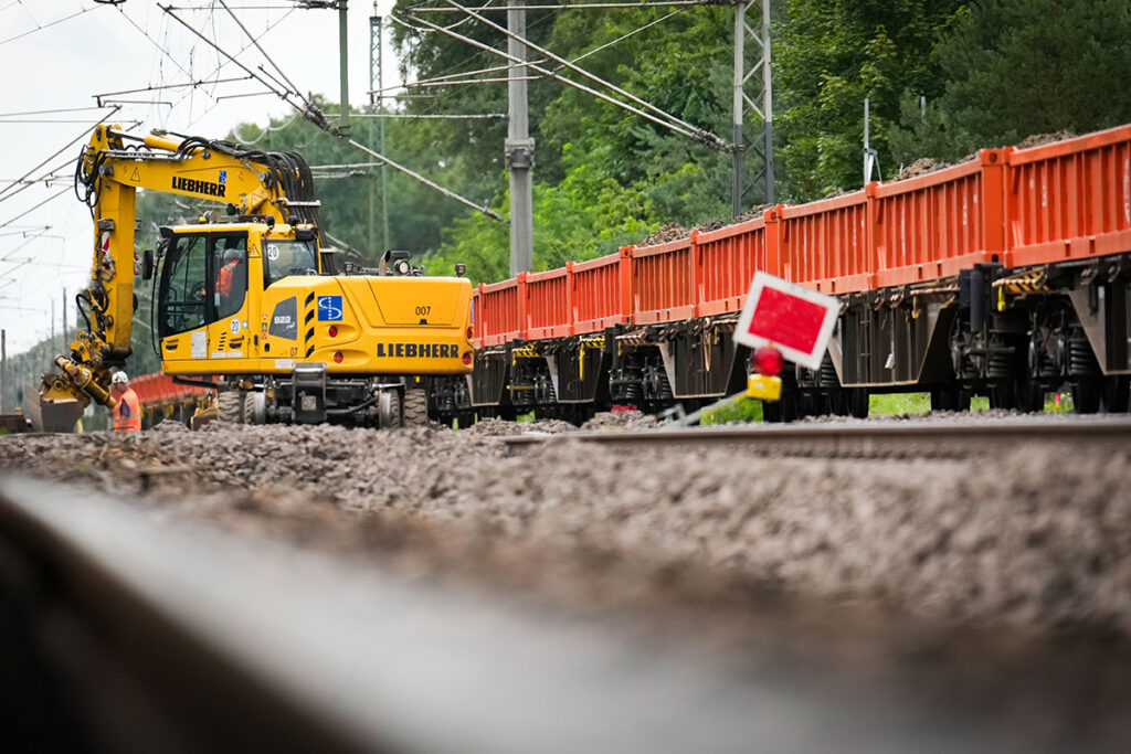 Ein Kran und Schotterwagen stehen auf einem Gleis.