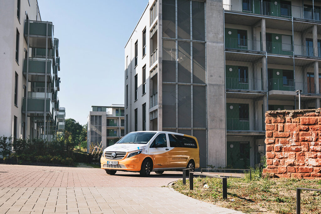 Ein Kleinbus steht vor mehrstöckigen Häusern.