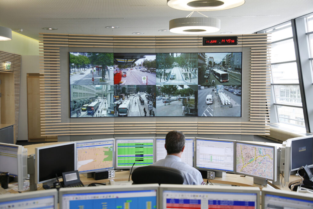 Eine Person sitzt in einem Raum vor vielen Computer-Bildschirmen.