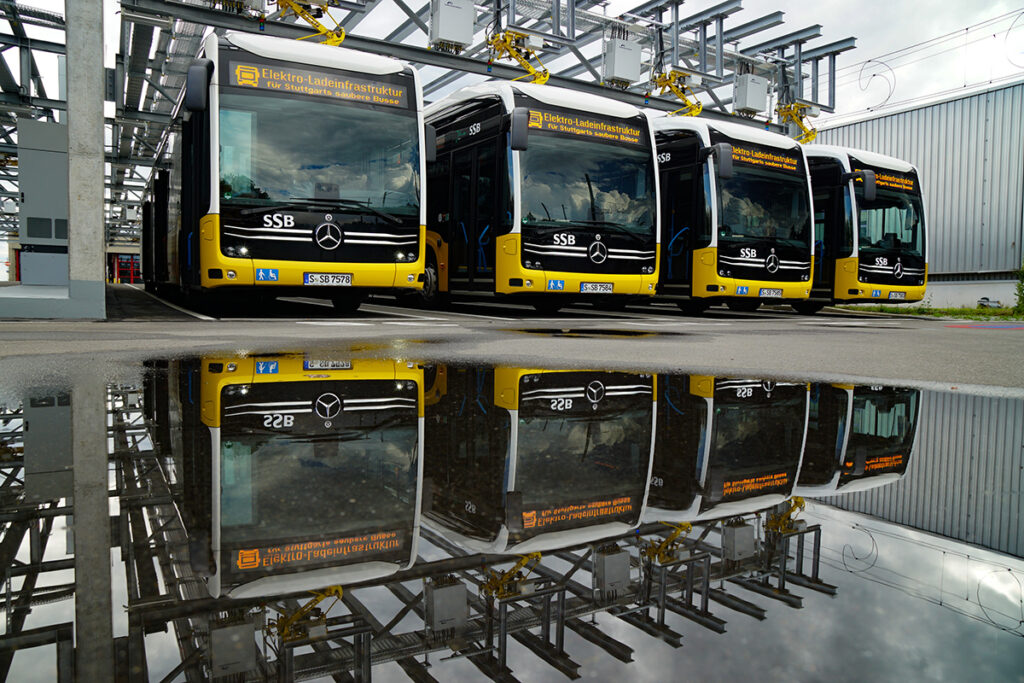 Elektrobusse stehen nebeneinander unter einer Ladeanlage.