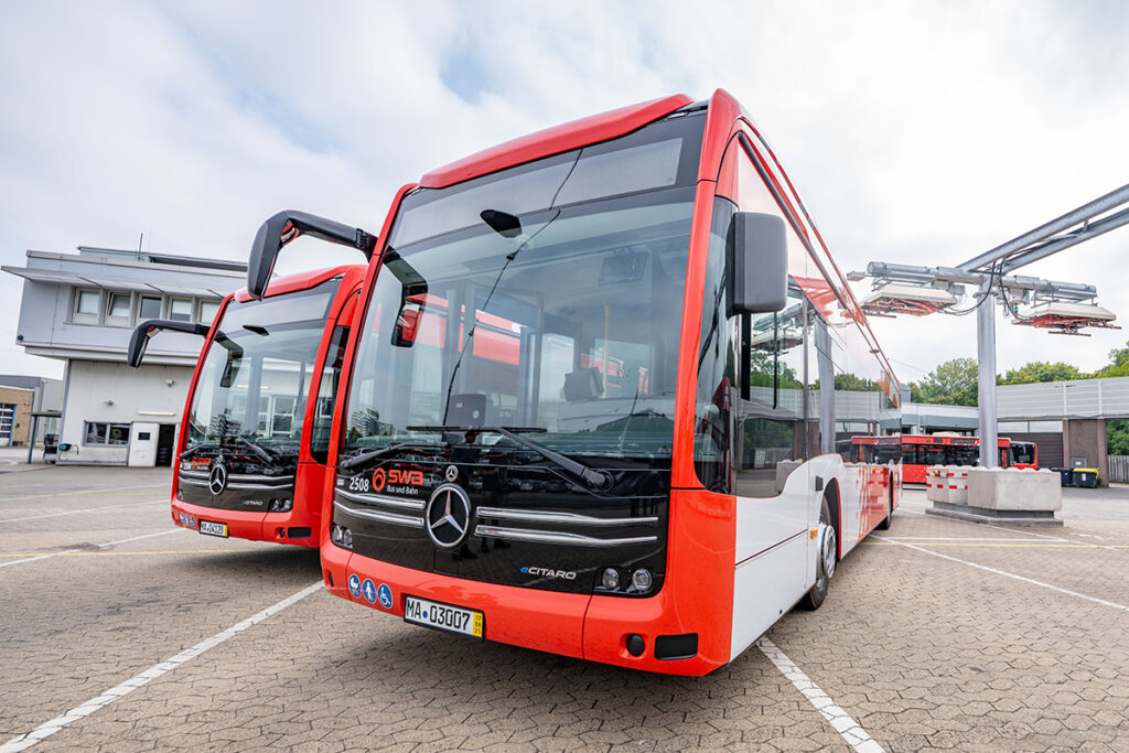 Zwei Busse stehen neben einer Ladestation.