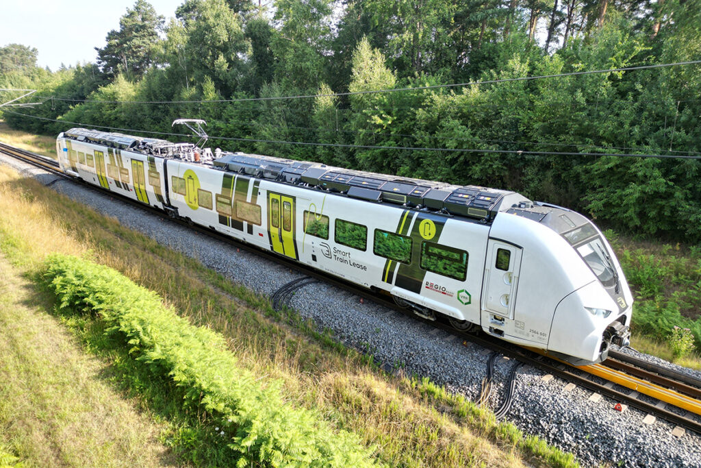 Ein Batteriezug fährt durch einen Wald.
