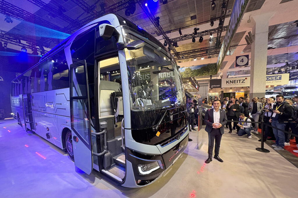 Viele Personen stehen neben einem elektrischen Reisebus.