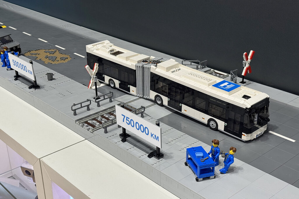 Ein Modellbus fährt auf einer Straße über einen Bahnübergang.