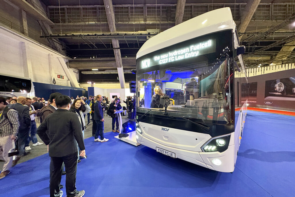 Besucher stehen in einer Messehalle neben einem Bus von MCV.