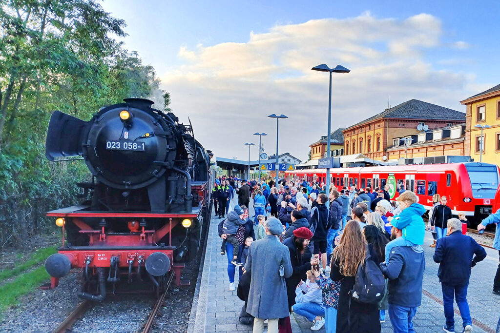 Eine Dampflok steht an einem Bahnsteig, auf dem viele Menschen stehen.