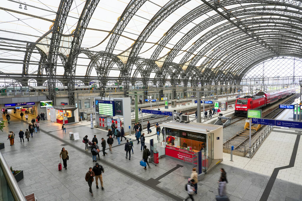 Blick in eine Bahnhofshalle mit Zügen und Menschen.