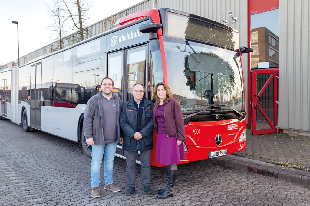 Drei Personen stehen vor einem Bus.