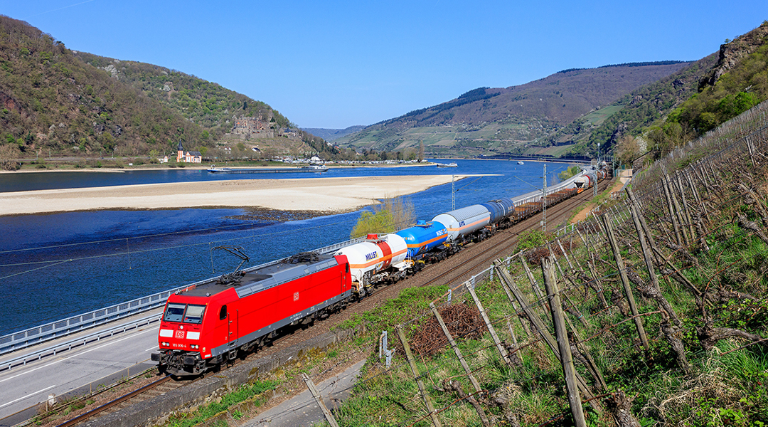 Ein Güterzug fährt durch ein Tal an einem Fluss entlang.