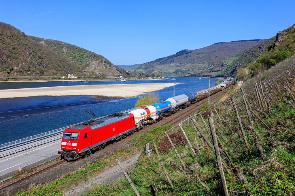 Ein Güterzug fährt durch ein Tal an einem Fluss entlang.