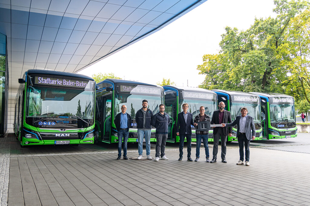 Mehrere Personen stehen vor Bussen unter einem Dach.