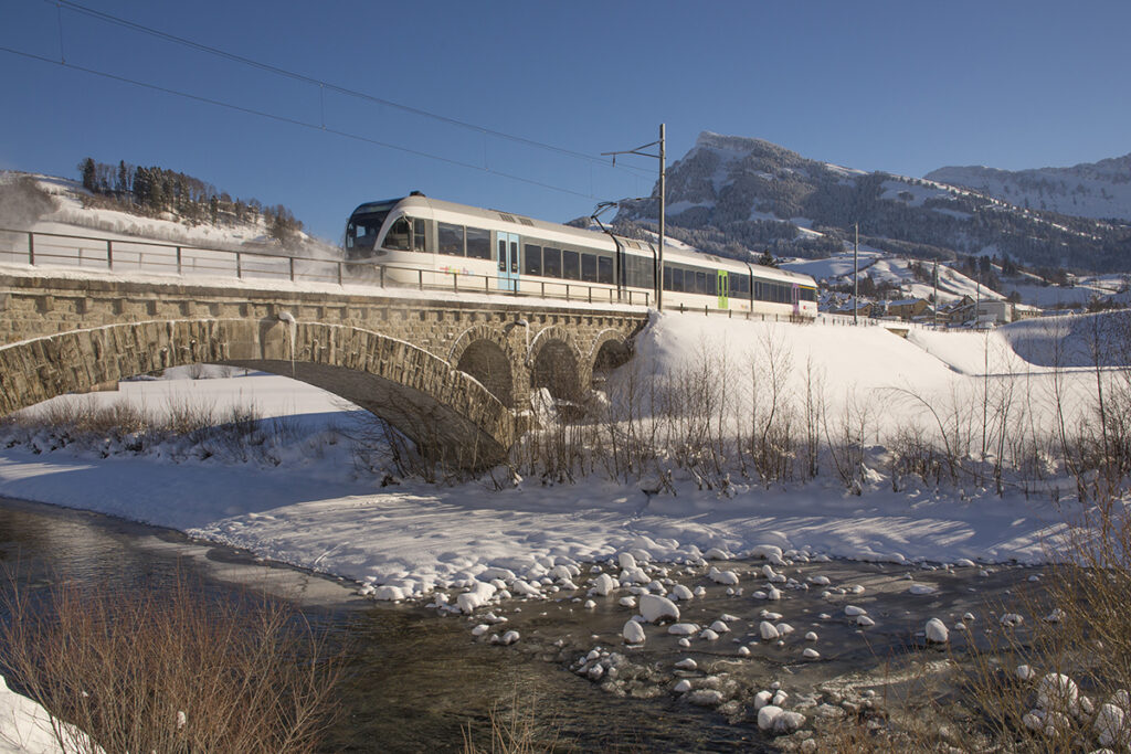 Ein Zug fährt in einer verschneiten Landschaft über eine Brücke.
