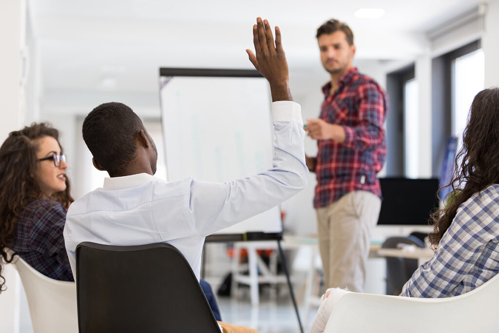 Vier Personen in einem Raum, ein vorne sitzende Person hebt den Arm.