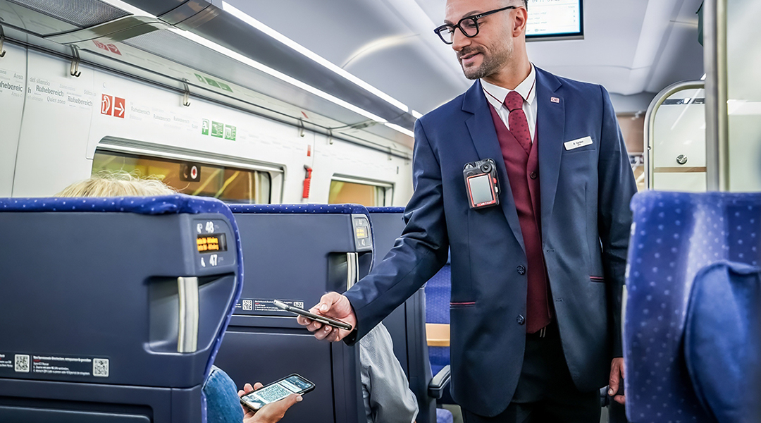 Ein Schaffner prüft in einem Zug die Fahrkarte eines Fahrgastes.