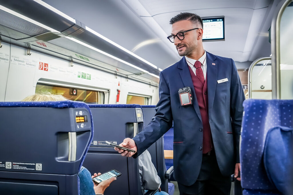 Ein Schaffner prüft in einem Zug die Fahrkarte eines Fahrgastes.